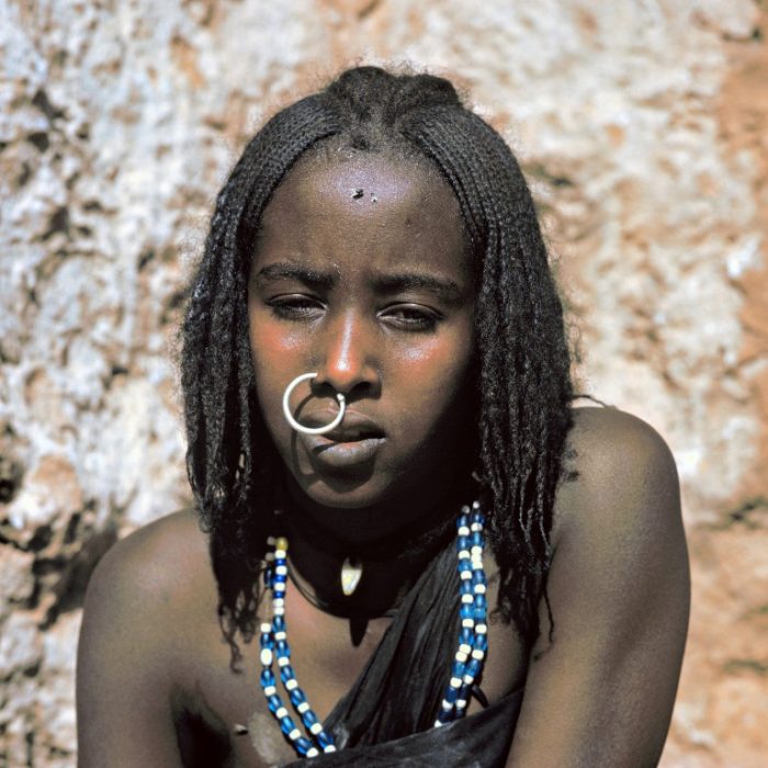 Le serpent et la mouche. Jeune femme Kanouri dans la région du Kaouar (désert du Ténéré, Niger). Elle porte l’anneau nasal traditionnel représentant un serpent qui se mord la queue. Quant à la mouche qui orne son front, elle appartient hélas à une engeance omniprésente sous ces latitudes…