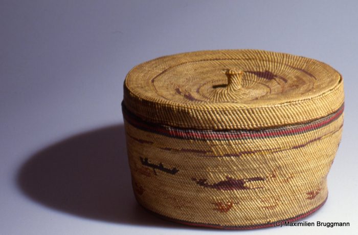 85 A small, densely woven basket with lid. The material is dyed and undyed sweet grass, interwoven to create a scene with water birds and a whaling canoe hunting a killer whale. The basket was acquired from the Makah in 1880. (24 cm; VM)