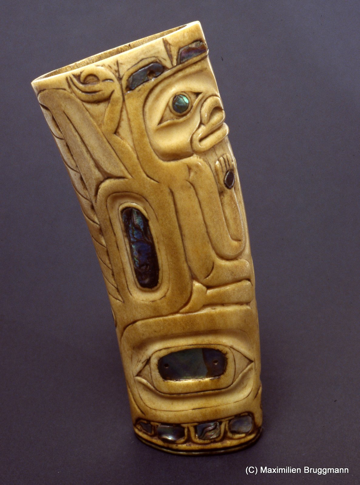 32 This drinking vessel is carved out of the tusk of a walrus and decorated with haliotis shell. The partially visible figure is probably an anthropomorphic bear. The cup originated in the same region as the salmon charm described above. (14 cm; NMM)