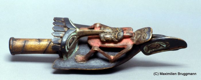 34 The Tsimshian may have been the first to make raven dance raffles. This example represents a widely disseminated model: On die back of a raven sits a man whose tongue is being pulled out by a frog, which is, in turn, being seized by a kingfisher. The underside of the rattle shows a hawk. "Underside" is incorrect in-sofar as this was the side which was on top when a chief held the rattle in his hand. (28 cm; ASM)