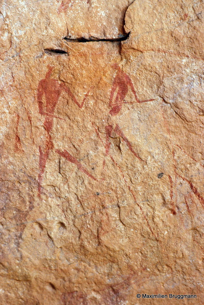 303 Ouan Ouksem (Tadrart). — Abri. Deux person¬nages marchant (en discutant ?) peints à l'ocre rouge. Celui de gauche, du sommet de la tête aux pieds mesure 0,15 m de hauteur.